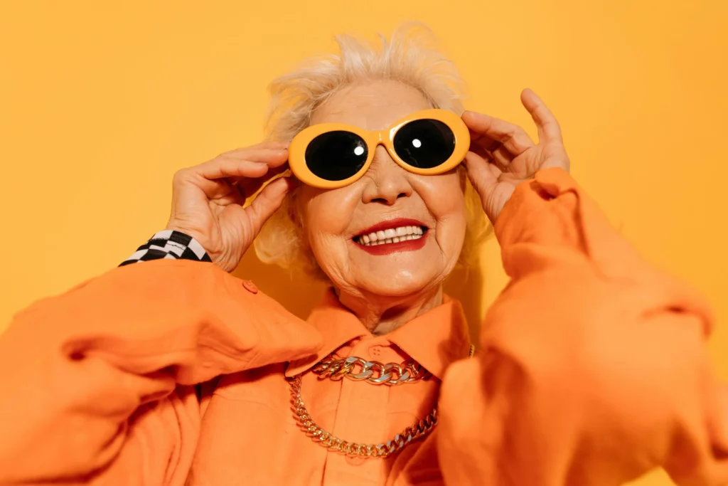 Fit im Alter mit 100 Jahren - eine fidele Alte in Orange mit Sonnenbrille